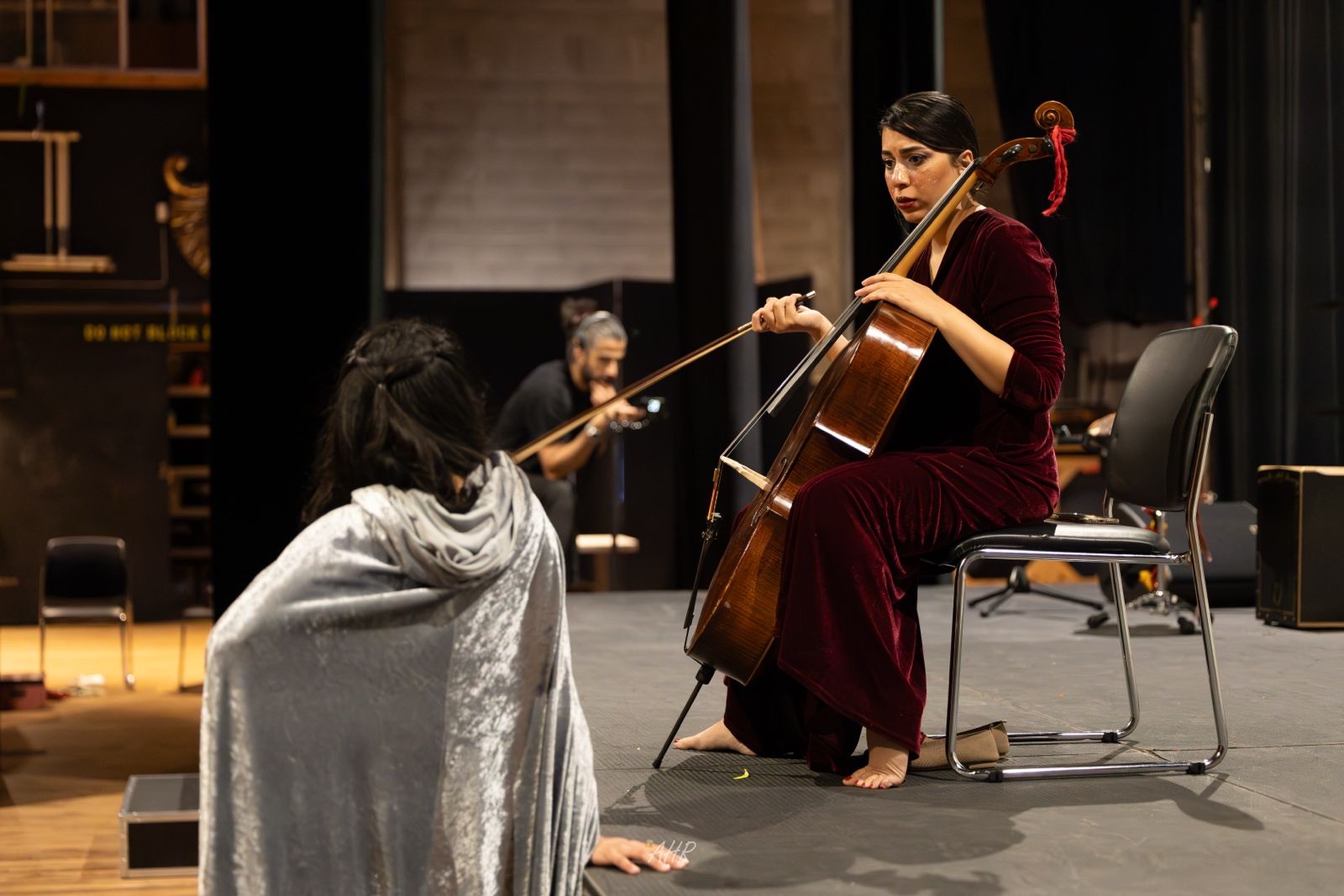 Blood Wedding — Act VI: the cellist in a red velvet dress playing to a cloaked figure seated on the stage floor