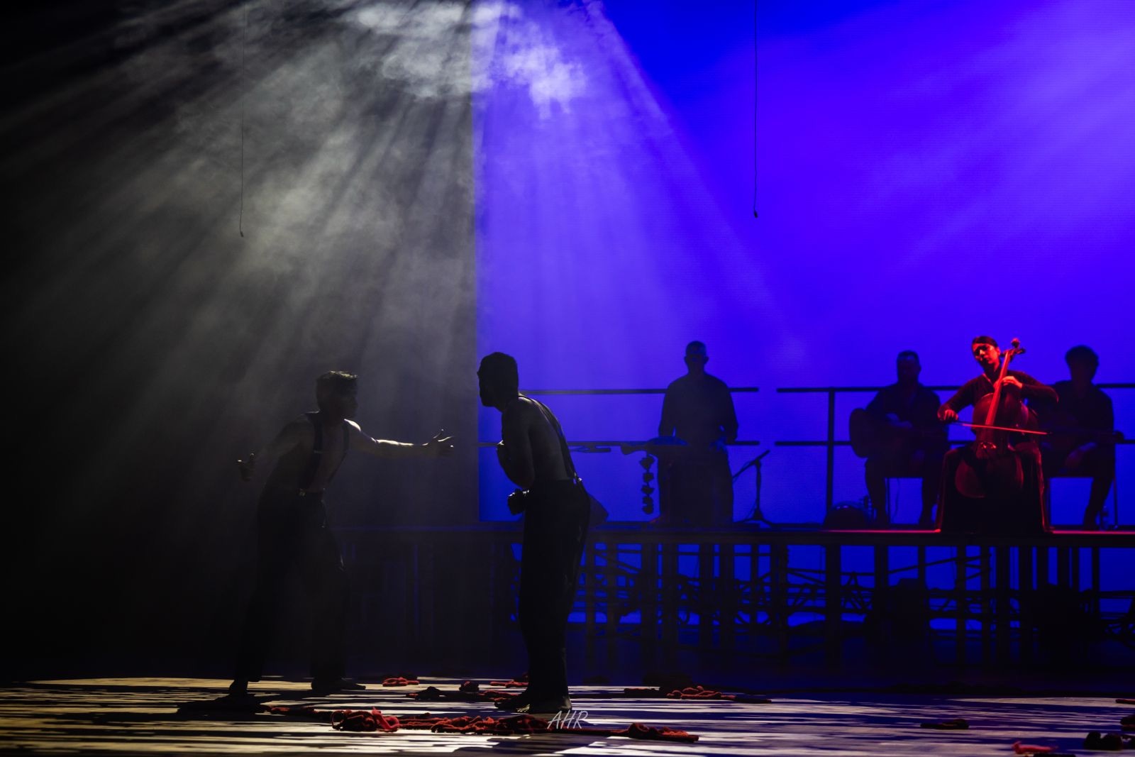 Blood Wedding — Act VI: two actors facing each other in shafts of light through haze, the band playing on the platform behind them