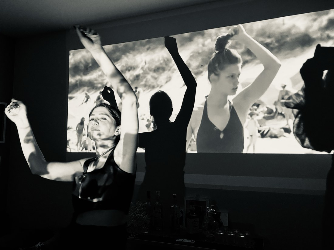 People dancing with raised arms in front of a projected film of a woman on a beach