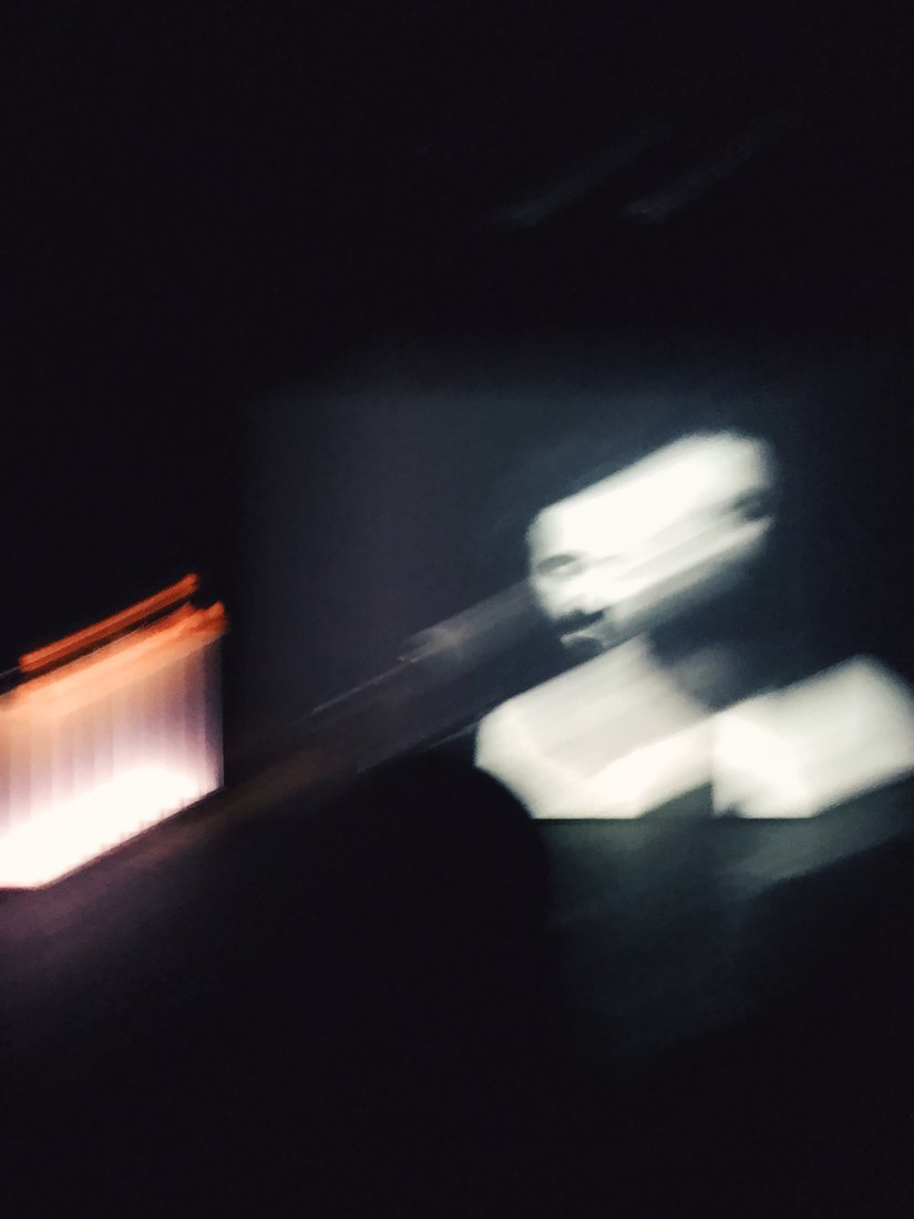 A blurred projection of a face in a dark room, a strip of warm light at the edge of the frame