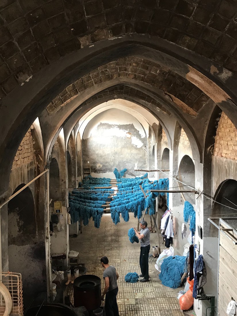 A vaulted dye-house hung with skeins of bright blue wool, two men working among them